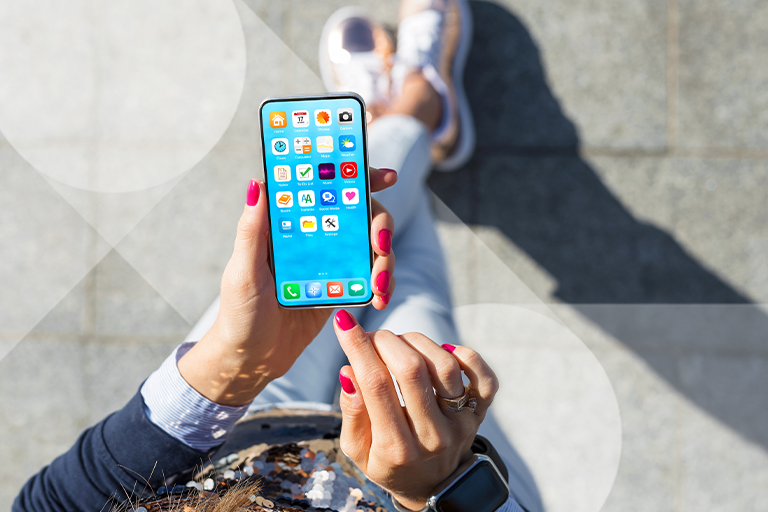 Overhead view of woman standing using her phone. We see a screen full of apps and in the background, her crossed sneakers on the ground behind it.