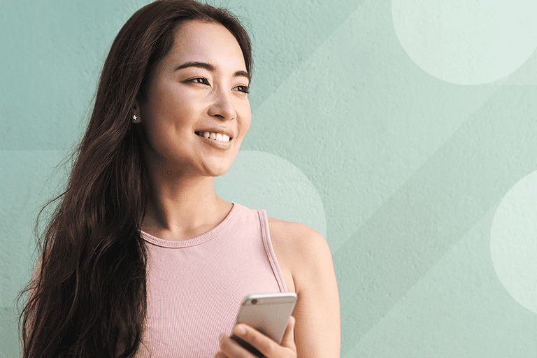 Stock photo of Asian woman smiling while holding phone to celebrate Women's History Month and International Women's Day