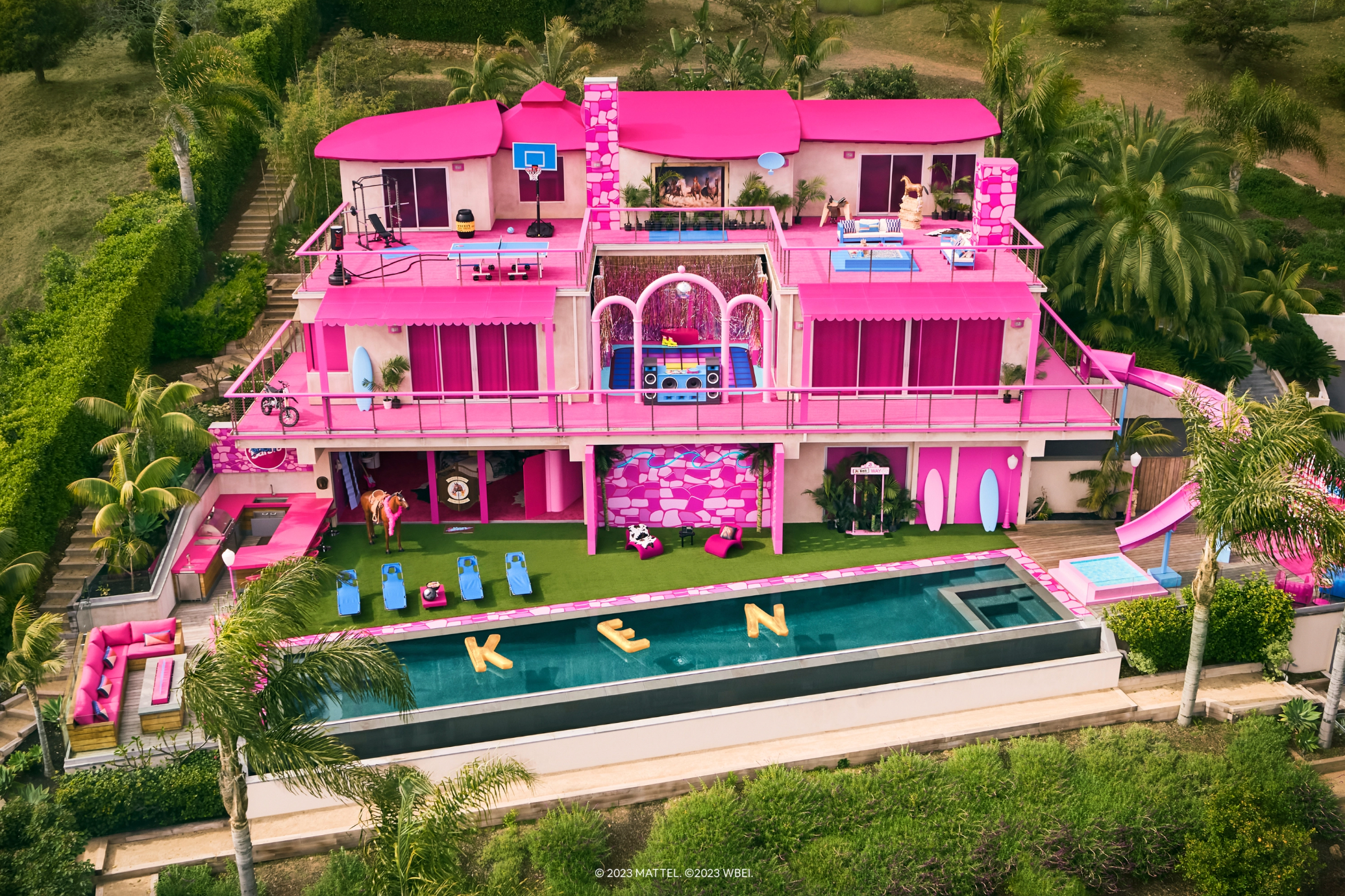 A bright pink house features a swimming pool in the front with floating letters K, E and N.